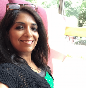 A photo of Priya smiling outside with glasses on top of her head.